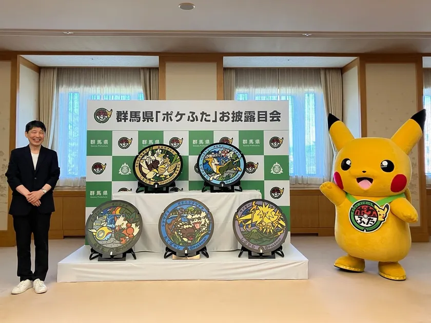 Pikachu mascot waving beside five Poké Lids at Gunma’s unveiling ceremony