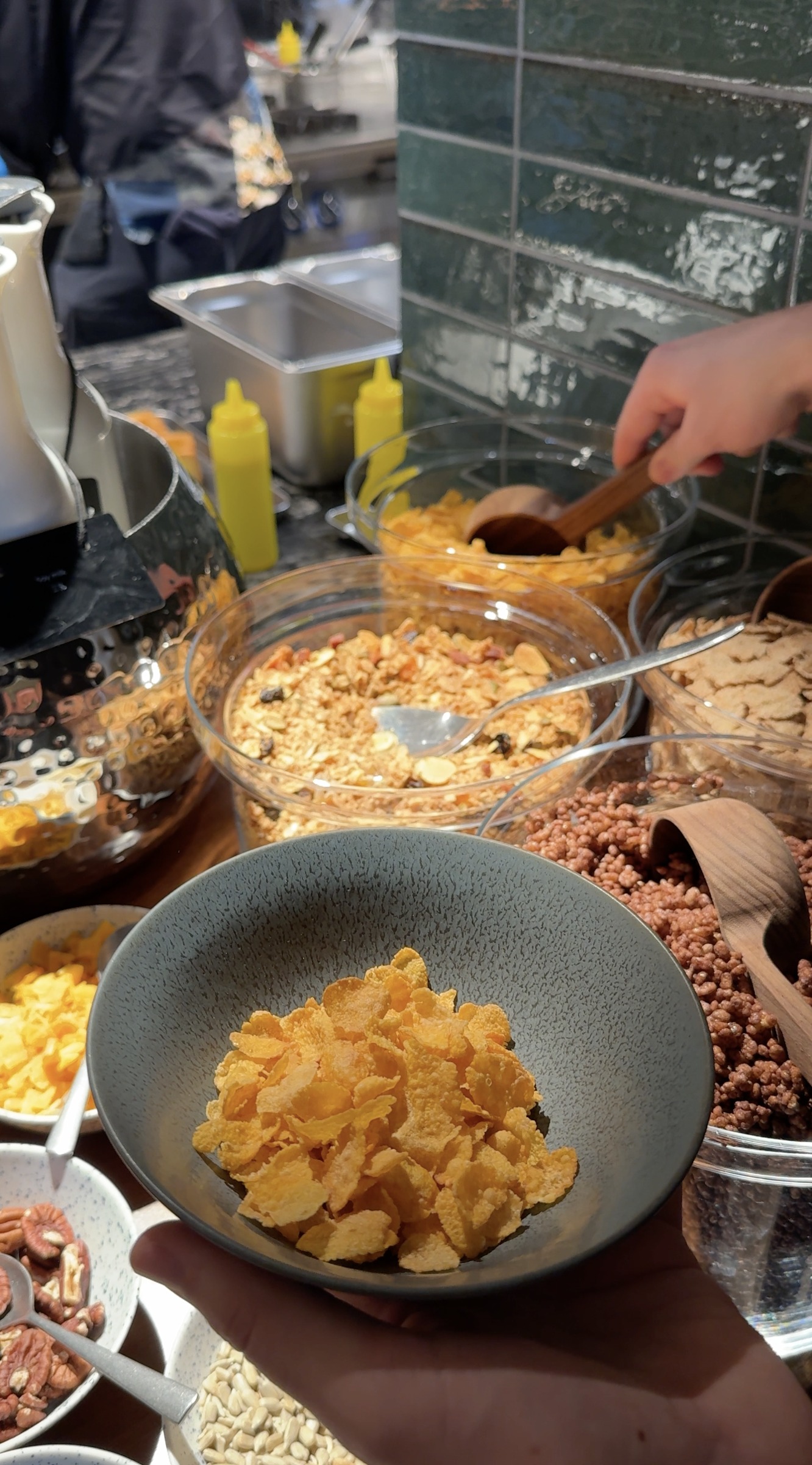 A bowl of cornflakes beside the cereal and granola choices at breakfast