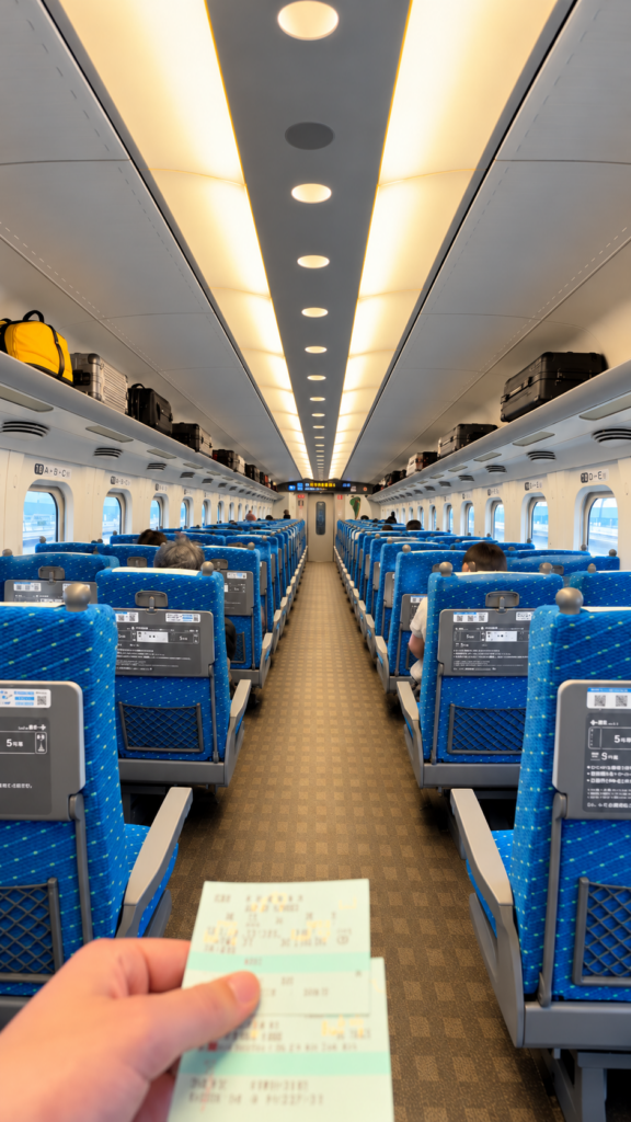 Suitcases and bags on overhead racks above blue Shinkansen seats
