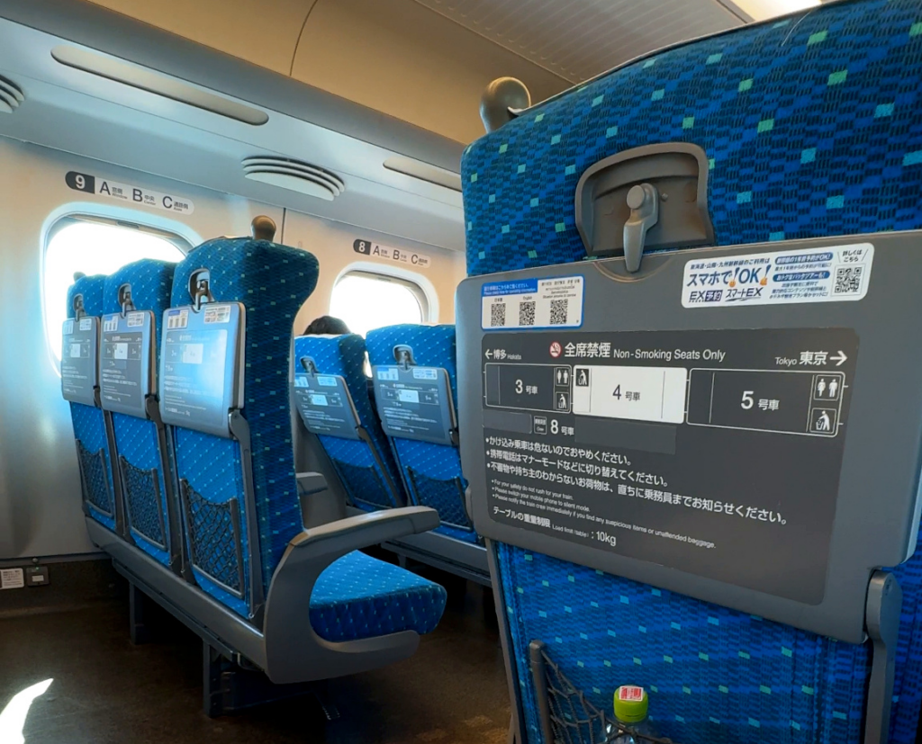 Blue Shinkansen seats with folded tray tables, armrests and the space between rows